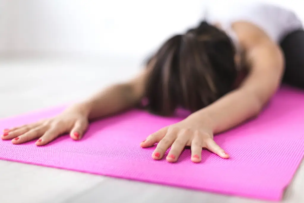 A student resting in child's pose with arms extended on a pink mat