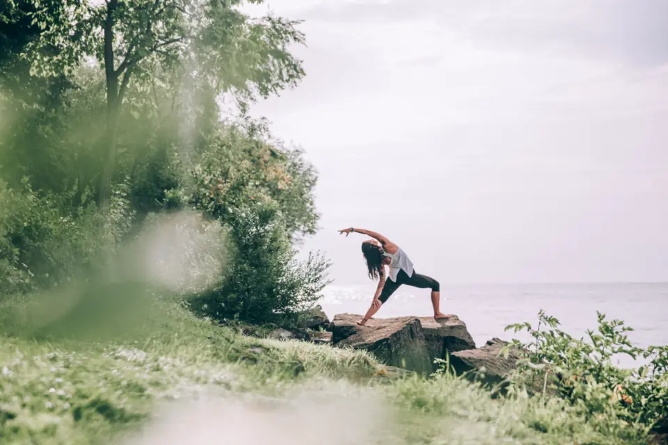 A woman in a side angle pose on a rock by the water, with her front knee bent