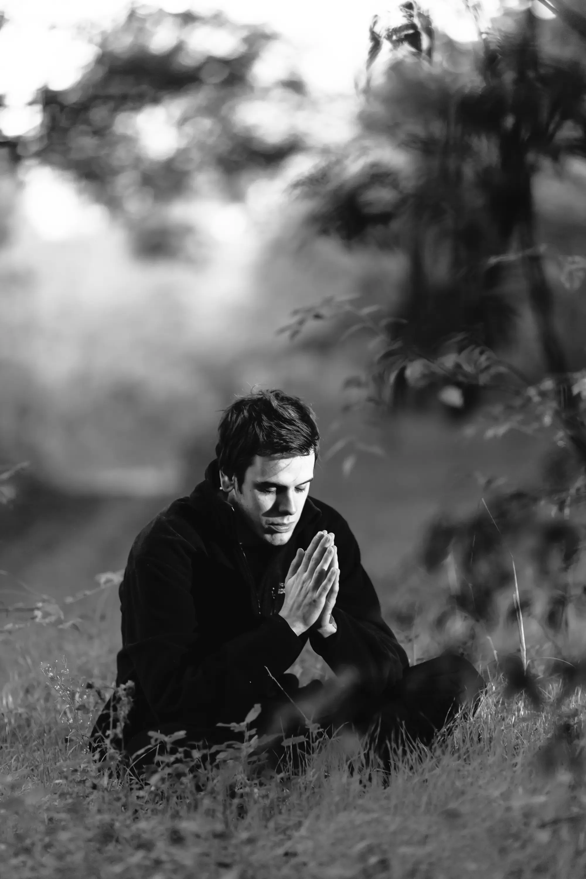 A man sitting quietly outdoors with his palms pressed together in front of his chest