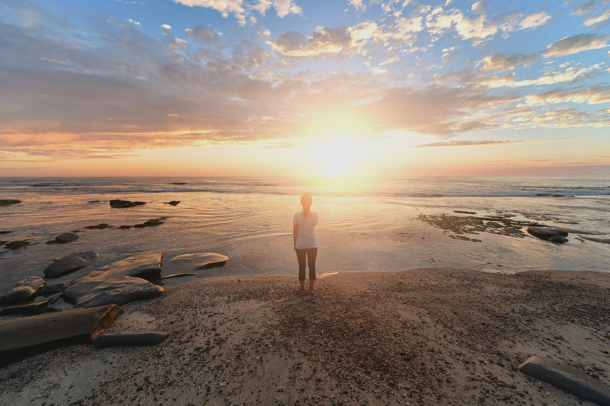 A woman standing on a rocky shoreline watching the sunrise